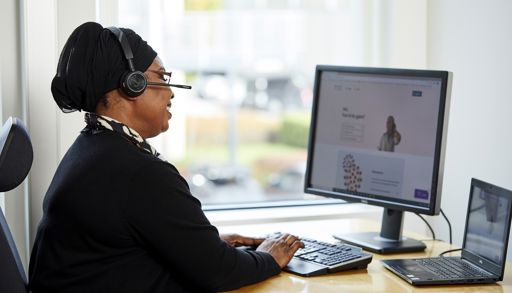En kvinne med hodetelefoner, som sitter ved et skrivebord med en datamaskin
