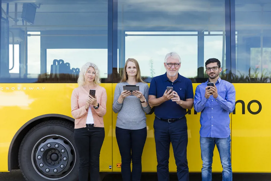 En gruppe mennesker som står foran en gul buss