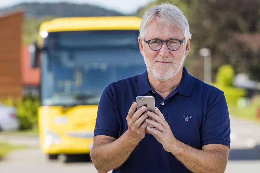 Mann med telefon foran buss