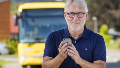 Mann med telefon foran buss