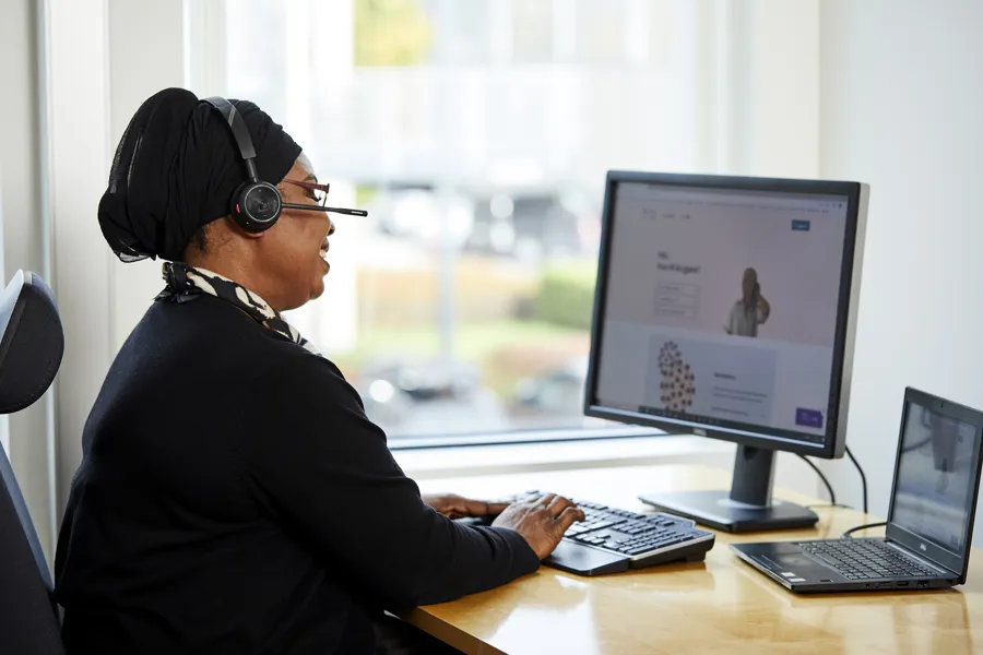 En kvinne med hodetelefoner og sitter ved et skrivebord med en datamaskin