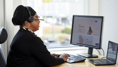 En kvinne med hodetelefoner og sitter ved et skrivebord med en datamaskin