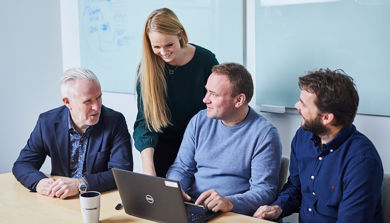 En gruppe mennesker som sitter rundt et bord og ser på en bærbar datamaskin