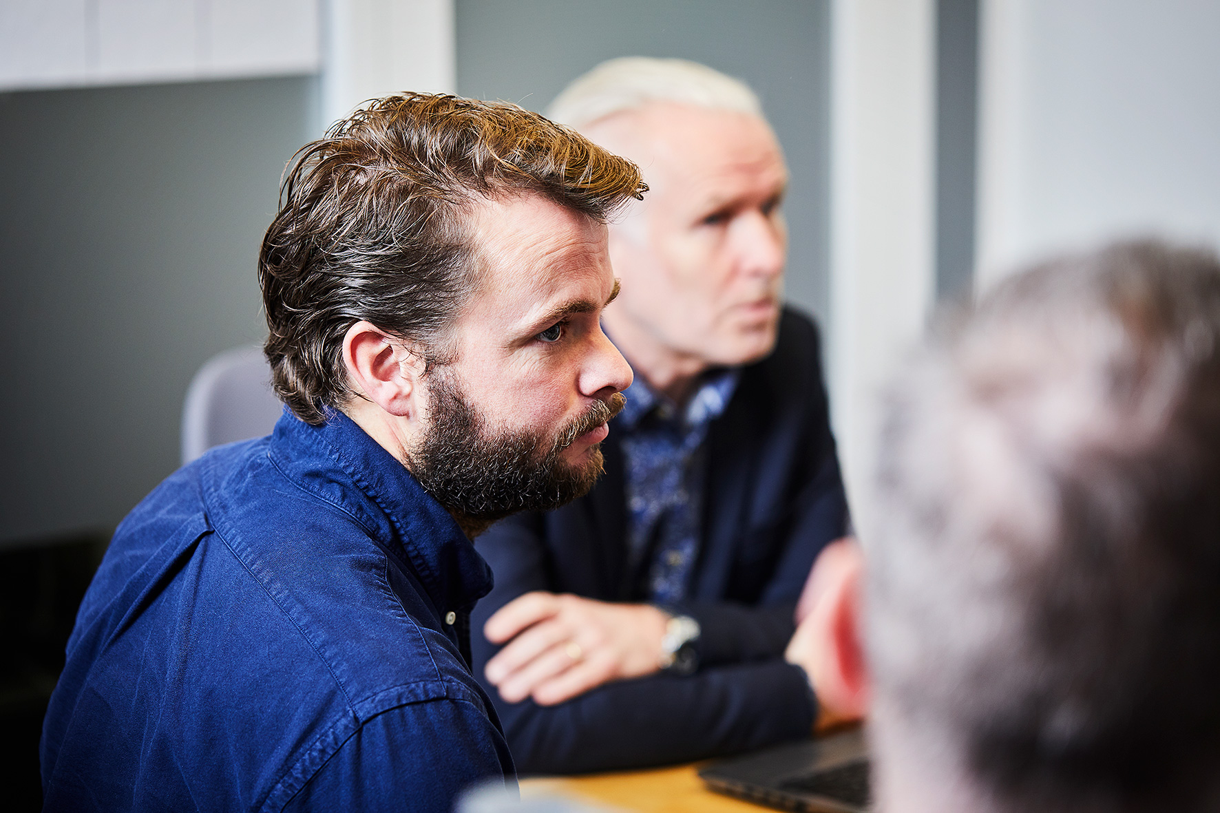 En mann med skjegg som sitter ved et bord med andre menn